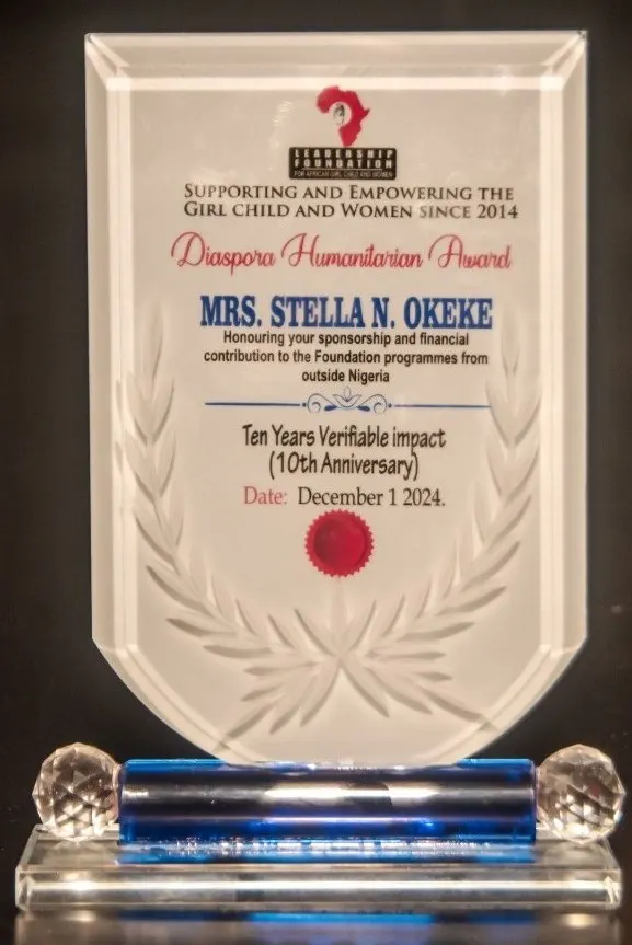 A clear glass award plaque with blue accents, presented by the 'Leadership Foundation for African Girl Child and Women'. The award is titled 'Diaspora Humanitarian Award' and is presented to 'Mrs. Stella N. Okeke' for her sponsorship and financial contribution. It commemorates 'Ten Years Verifiable impact (10th Anniversary)' and is dated 'December 1, 2024'.